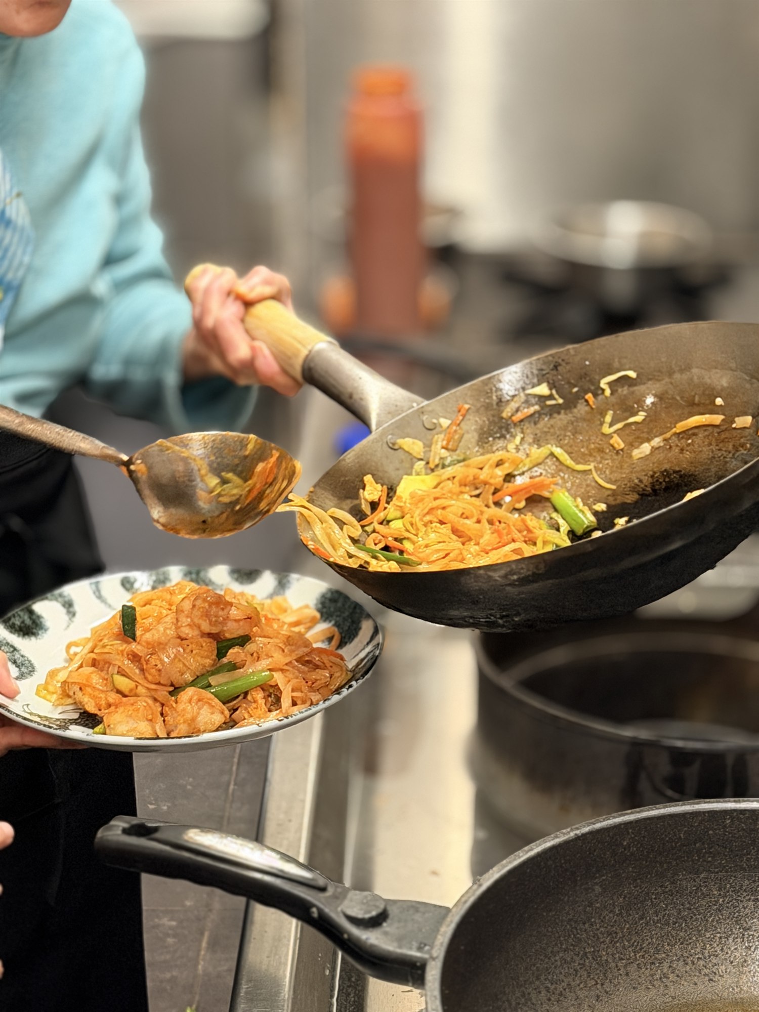 Noedels worden vanuit de wok op een bord geschept